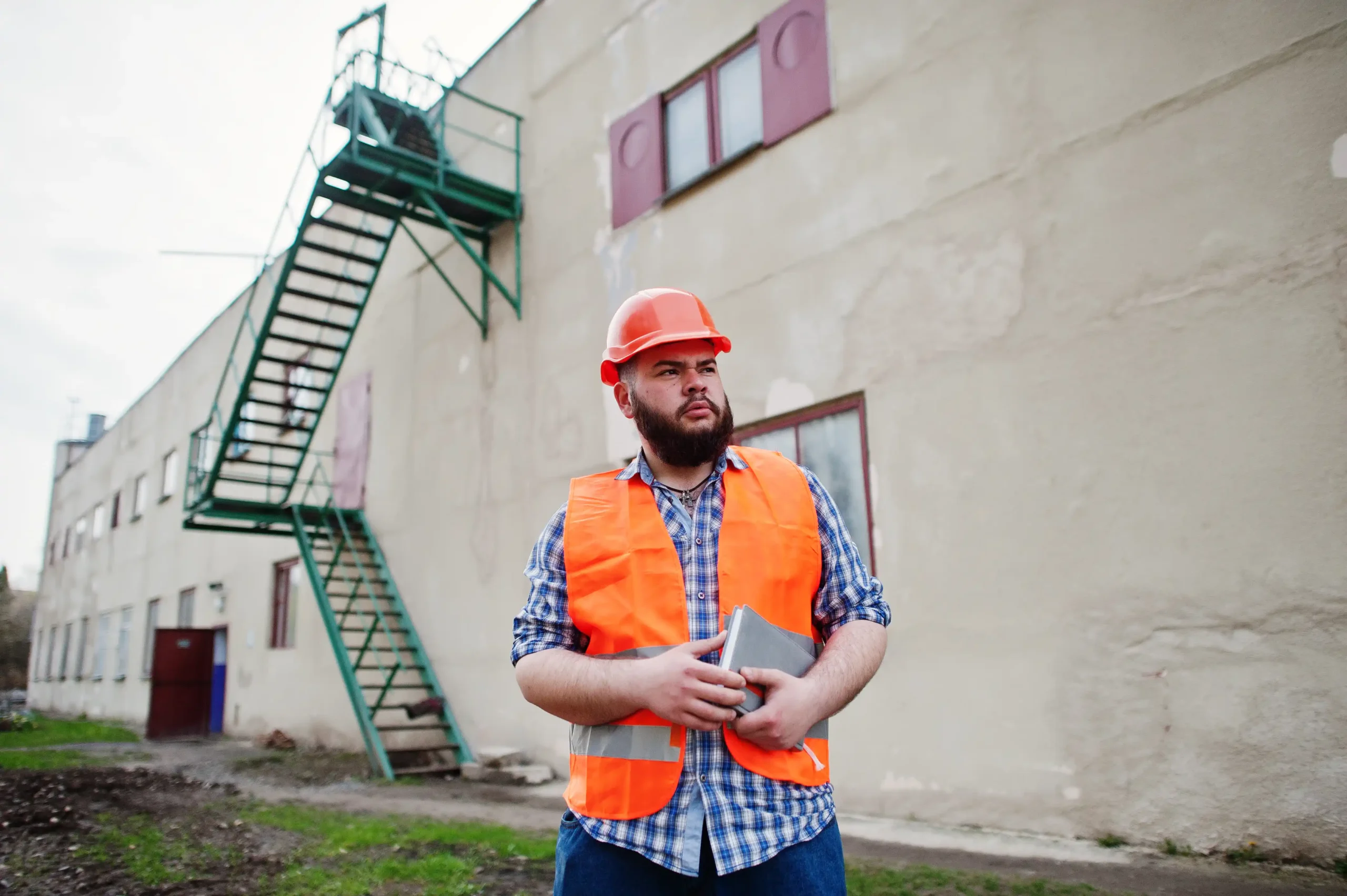 A man in an orange vest is standing in front of a building.